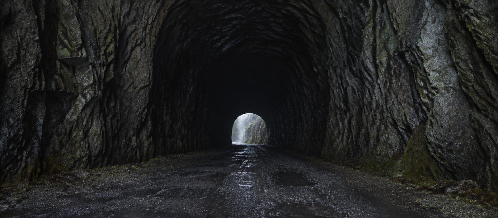 De donkere mond van een tunnel door rots, met vaag daglicht aan het verre einde